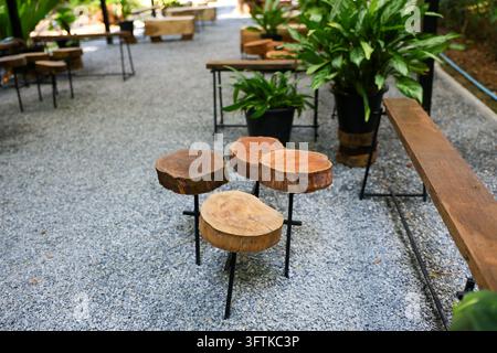 Ein Straßencafé mit Sitzgelegenheiten aus Baumstümpfen, Kiesboden, Topfpflanzen und rustikalen Tischen, das eine entspannte Gartendining-Atmosphäre schafft Stockfoto