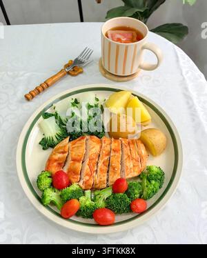 Ein gesundes gegrilltes Lachsgericht, serviert mit Brokkoli, Kirschtomaten, Blattgemüse und gekochten Kartoffeln auf einem Keramikteller Stockfoto