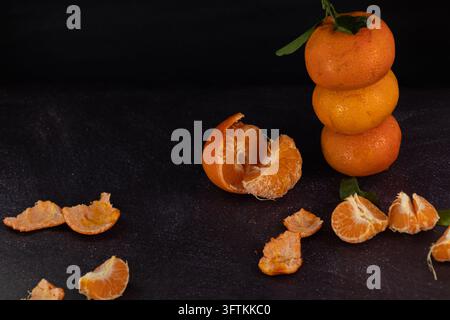 Frische Mandarinen, die auf einem rustikalen Hintergrund gestapelt sind, mit geschälten Mandarinen, die verstreut herumliegen. Dunkles Essen Stockfoto
