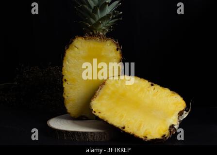 Ananas in der Hälfte geschnitten auf einem Holzblock auf einem rustikalen Hintergrund, duftende und süße tropische Frucht. dunkles Essen Stockfoto
