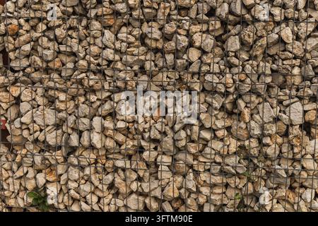 Gabionwand aus Kalksteinbrocken, die in einem Drahtgitterzaun gehalten werden, vollflächiger strukturierter Hintergrund Stockfoto