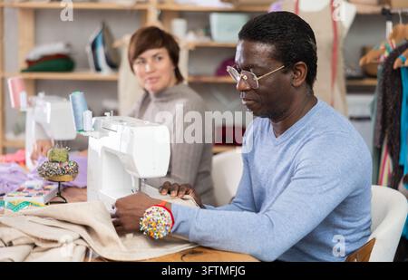Zwei engagierte Modedesigner, Frau und Mann, nähen maßgeschneiderte Kleidungsstücke an Maschinen, konzentrieren sich auf Präzision und Detailgenauigkeit und setzen kreative Visionen um Stockfoto