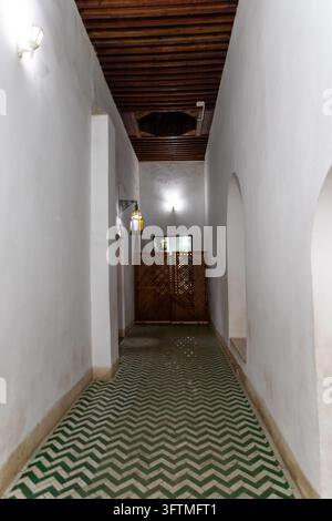 Ein langer weißer Korridor in einem marokkanischen Palast mit einem auffälligen grün-weißen Chevron-Fliesenboden unter einer dunklen Holzdecke in Marrakesh.... Stockfoto