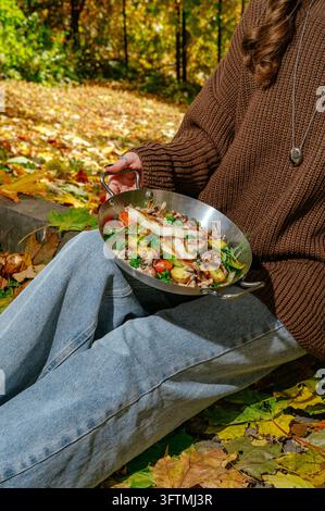 Frau mit Pfanne voller gegrilltem Fisch und Gemüse im Herbst Stockfoto