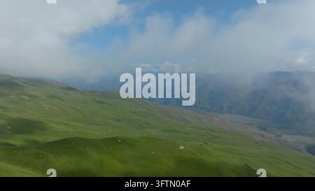Ein weitläufiges Luftbild fängt üppige Hochländer, einen sich windenden Feldweg und Wolkenschatten ein, während ferne Bergschichten in Dunst über Dages verschwinden Stockfoto