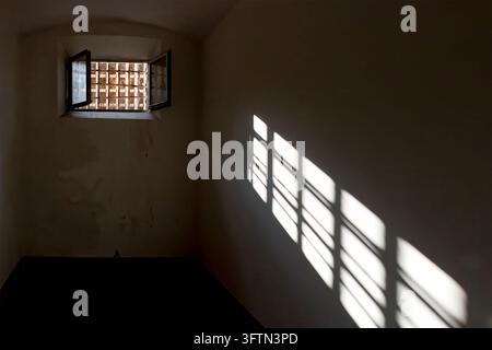 Licht dringt durch das Fenster einer Gefängniszelle mit Gitterstäben und wirft einen dramatischen Schatten an die Wand Stockfoto
