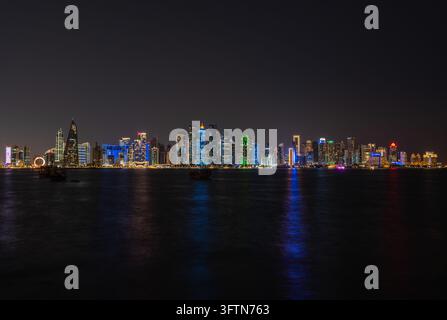 Doha, Katar - 22. Januar 2026: Weite Langzeitbelichtungs-Nachtsicht der Skyline von Doha von der Corniche aus, die traditionell verankerte Daus zeigt. Stockfoto