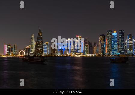 Doha, Katar - 22. Januar 2026: Mittlere Telefoto-Langzeitbelichtung einer Nachtsicht der Skyline von Doha von der Corniche aus, die traditionelle Daus betont. Stockfoto