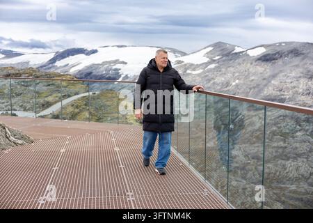 Reifer Mann steht auf einer Bergaussichtsplattform mit Blick auf schneebedeckte Gipfel Stockfoto