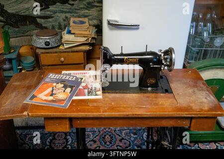 Vintage-Nähmaschine auf Holztablett mit Retro-Zeitschriften in gemütlicher Werkstattinnenausstattung Stockfoto