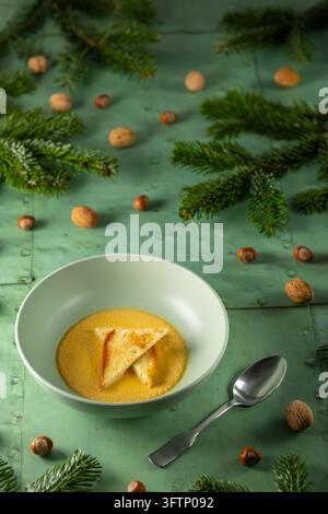 Warme Kürbissuppe in einer Schüssel mit gerösteten Croutons, umgeben von festlichen Tannenwedeln und Nüssen Stockfoto