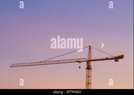 Gelber Turmkran gegen Abendhimmel mit Mondsichel. Stockfoto