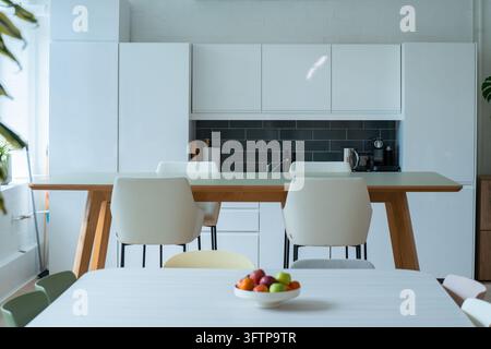 Ansicht eines modernen Büroküchenbereichs mit einem langen Holztisch, weißen Stühlen und einer Schüssel mit frischem Obst im Vordergrund, London, Vereinigtes Königreich Stockfoto