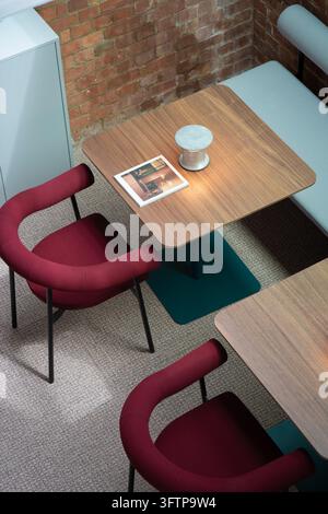 Ansicht eines modernen Bürointerieurs mit Holztischen und roten Stühlen vor einer Ziegelwand in London, Vereinigtes Königreich. Stockfoto
