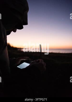 Mann bedient eine Drohnenfernbedienung im Freien bei Sonnenuntergang nahe der Küste. Stockfoto