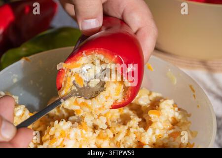 Eine Person hält eine leuchtend rote Paprika, die mit einer gewürzten Füllung aus Reis, Hackfleisch und Karotten über einer Rührschüssel in hellem natürlichem Li gefüllt ist Stockfoto