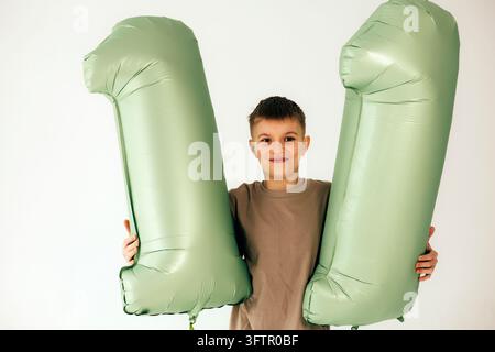 Zufriedener 11-jähriger Junge hält grüne Luftballons mit der Nummer 11 Stockfoto