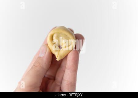 Hand, die einen rohen, handgemachten Tortellini-Teigklößchen hält, isoliert auf weißem Hintergrund mit Kopierraum. Stockfoto
