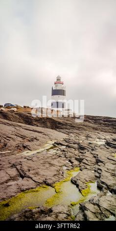 Hook Head, County Wexford, Irland – 08. September 2024: Blick auf den Hook-Leuchtturm, der an der felsigen Küste mit Gezeitentümpeln und moosbewachsenen Steinen steht Stockfoto