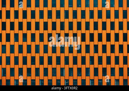 Helle orangefarbene Verkleidung umgibt versetzte Reihen dunkler rechteckiger Fenster an der Fassade eines Bürogebäudes. Feine vertikale Rippen verleihen der Wiederholung Struktur Stockfoto