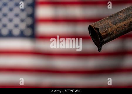 Rohes schwarzes Öl tropft von einem rostigen Metallrohr mit amerikanischer Flagge im Hintergrund, Nahaufnahme. Unscharfer USA-Flaggenhintergrund für die amerikanische Erdölindustrie Stockfoto