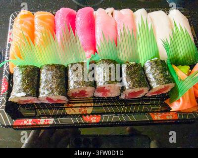 Farbenfrohes Takeaway-Sushi-Set bestehend aus Nigiri und Maki in einer Plastikbox, dekoriert mit grünem Plastik-„Gras“ Stockfoto