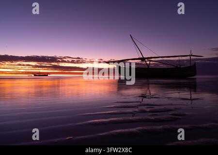 Ein kleines traditionelles afrikanisches Boot ruht auf ruhigem, spiegelndem Wasser unter einem lila und orangefarbenen Sonnenuntergang bei Ebbe Stockfoto