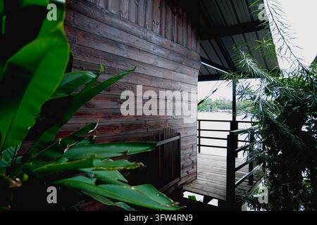 Tropfhütte aus Holz mit einem malerischen Balkonblick und lebendigen grünen Blättern im Vordergrund, friedliche Flussufer-Ferienhausarchitektur Stockfoto