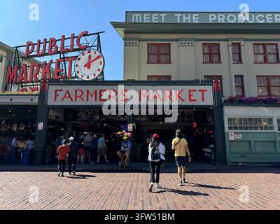 Besucher betreten den Pike Place Market unter dem Schild „Farmers Market“ und der ikonischen Public-Market-Uhr im Stadtzentrum von Seattle, Washington, USA. Stockfoto