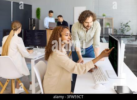Entwicklerin zeigt während der Codereview in einem hellen modernen Büro auf den Monitor Stockfoto