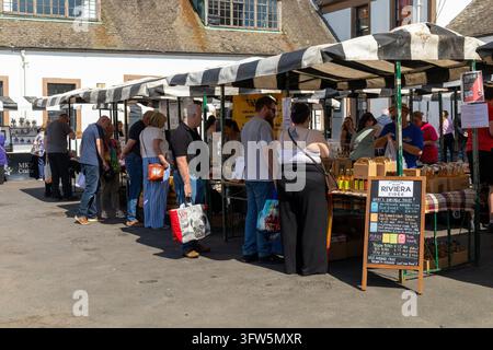 Ayr, UK - 21. Juni 2026: Kunden stehen an Marktständen unter schwarz-weiß gestreiften Markisen an einem sonnigen Tag; die Kreidetafel zeigt lokale Cider und Stockfoto