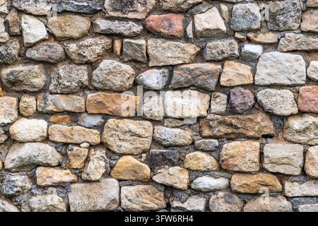 Hintergrundtextur einer rustikalen antiken Steinmauer, gebaut mit unregelmäßigen Natursteinen und Mörtel Stockfoto