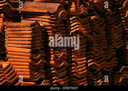 Verwitterte Terracotta-Dachziegel ordentlich in dichten vertikalen Stapeln gestapelt, beleuchtet von warmem Sonnenlicht mit tiefen natürlichen Schatten. Selektive Schärfentiefe. Stockfoto