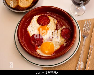 Beliebtes Gericht der spanischen Küche, gebratene Eier mit Chorizo-Würstchen und Tomatenpaste auf einem Teller im Café serviert Stockfoto