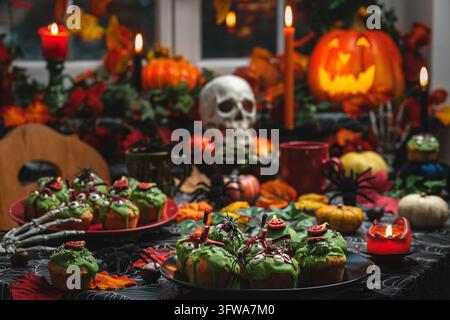Beängstigende Halloween-Cupcakes umgeben von Kerzen, Spinnen, Schädeln und Kürbissen Stockfoto