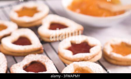 Eine Nahaufnahme zeigt stern- und herzförmige Linzer Kekse, gefüllt mit süßem Marmelade und mit Puderzucker bestäubt, auf einem Drahtgestell unter weichem natürlichem L Stockfoto