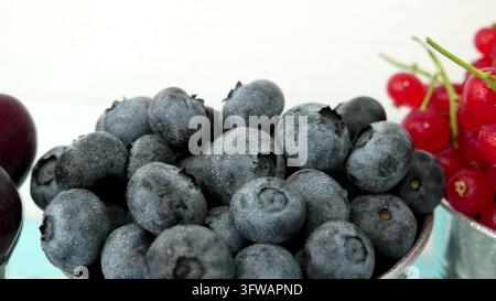 Eine Nahaufnahme von prallen Blaubeeren, die mit frischen Tautropfen bedeckt sind, gepaart mit lebhaften roten Johannisbeeren unter hellem natürlichem Licht, was ein frisches, gesundes Stockfoto