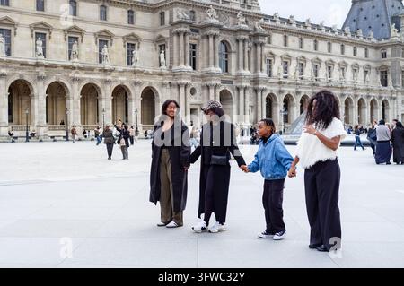 STILVOLLE FAMILIE GEHT IN PARIS, LOUVRE-MUSEUMGEBIET SONNTAG-REPORTAGE, PARIS, FRANKREICH, 2026: Eine stilvolle Mutter und ihre drei Kinder gehen Hand in Hand, lächeln und unterhalten sich, über den großen Hof eines europäischen Museums. INFO: Das Louvre-Gebiet verankert das kulturelle Herz von Paris und verbindet königliche Geschichte mit moderner Eleganz. Dominiert vom großen Museumspalast und seiner Glaspyramide, bietet der Bezirk den gepflegten Tuilerien-Garten und exklusive Einkaufsmöglichkeiten entlang der Rue de Rivoli. Stockfoto