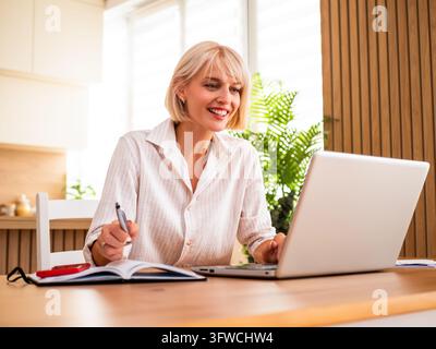 Selbstbewusste Frau konzentriert sich auf ihren Computer, während sie Online-Arbeit von zu Hause aus verwaltet. Stockfoto