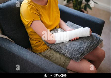 Kind mit verletztem Arm im Gips, das zu Hause in einem Sessel ruht Stockfoto