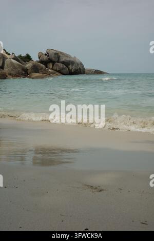 Ruhige Wellen, die an einem Sandstrand mit großen Felsbrocken heraufspülen Stockfoto