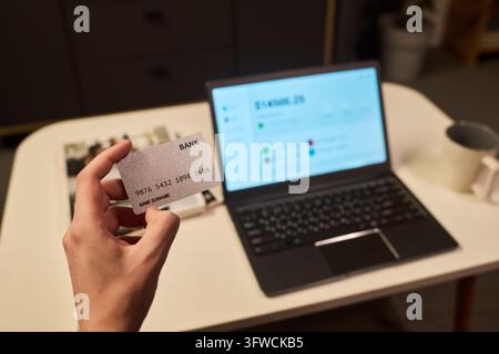 Hand eines Mannes, der eine Kreditkarte für Online-Banking auf einem Laptop hält Stockfoto