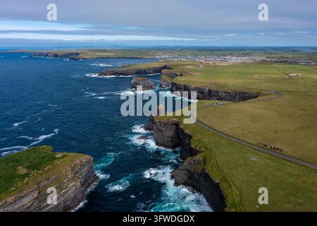 Luftaufnahme des wunderschönen und grünen Berges des berühmten Touristenzeichens Moher Cliff in Irland mit Meereswellen, die tagsüber unter Wolken auf Felsen treffen Stockfoto