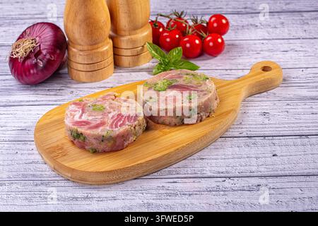 Thunfisch- und Brokkolischeiben auf einem Bambusschneidebrett. Frische Zutaten wie Kirschtomaten, rote Zwiebel und Basilikum umgeben das Gericht. Auf rustikalem Weiß platziert Stockfoto