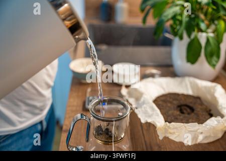 Heißes Wasser ergießt sich aus einem Wasserkocher auf Puer-Teeblätter in einem Glasinfuser. Die erste Infusion spült die Blätter vor dem Trinkbrühgut. Stockfoto