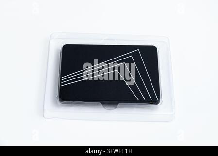 Eine schlanke schwarze Solid-State-Festplatte mit weißen geometrischen Linienakzenten ruht in ihrer klaren Plastikverpackung, bereit für digitale Speicherlösungen. Stockfoto