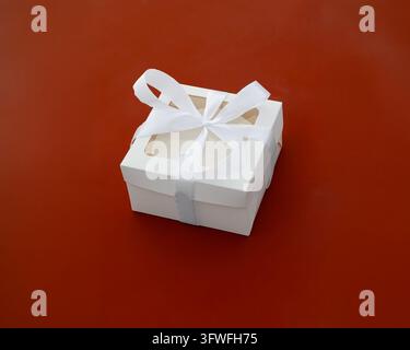 Geschlossene weiße Kuchenbox mit Kuchen darin und weißer Satin Schleife auf rotem Hintergrund Stockfoto