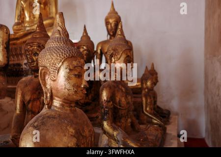Mittlere Nahaufnahme bei sanftem Tageslicht von mehreren antiken goldenen Buddha-Statuen mit verwitterten Patinas, die im Meditationszustand in einem Tempel sitzen. Stockfoto