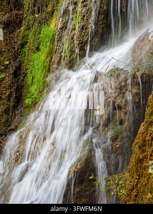 Kaskadierende Wasserfälle über moosbewachsenen Felsen - Eine wunderschöne Nahaufnahme eines natürlichen Wasserfalls mit glattem, fließendem Wasser, das über moosbedeckte Felsen kaskadiert Stockfoto
