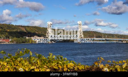 Blick auf die Portage Lake Lift Bridge, die das Wasser überquert, mit Herbstlaub auf den Hügeln im Hintergrund in Houghton, Michigan, Vereinigte Staaten. Stockfoto